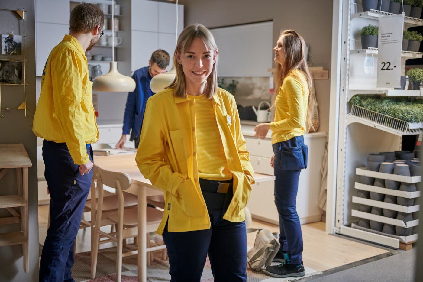 Varios empleados de IKEA con uniformes amarillos y azules sonríen dentro de una sección de exhibición de la tienda.